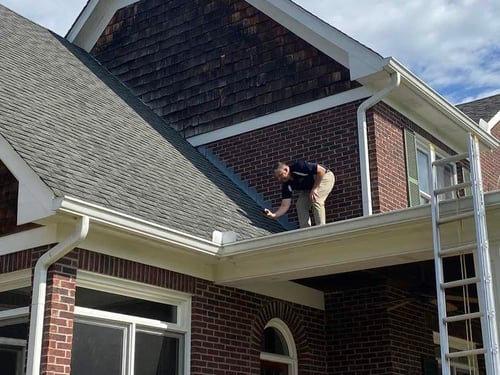 roofing contractor on roof taking pictures of storm damage to asphalt shingles