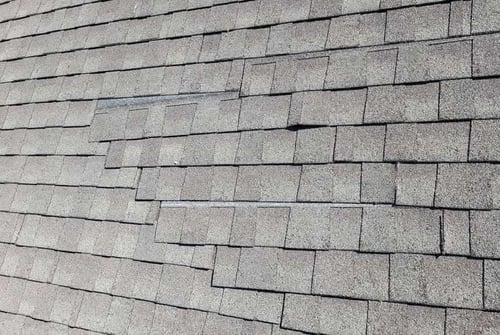 creased and lifted asphalt shingles caused by wind damage to a roof